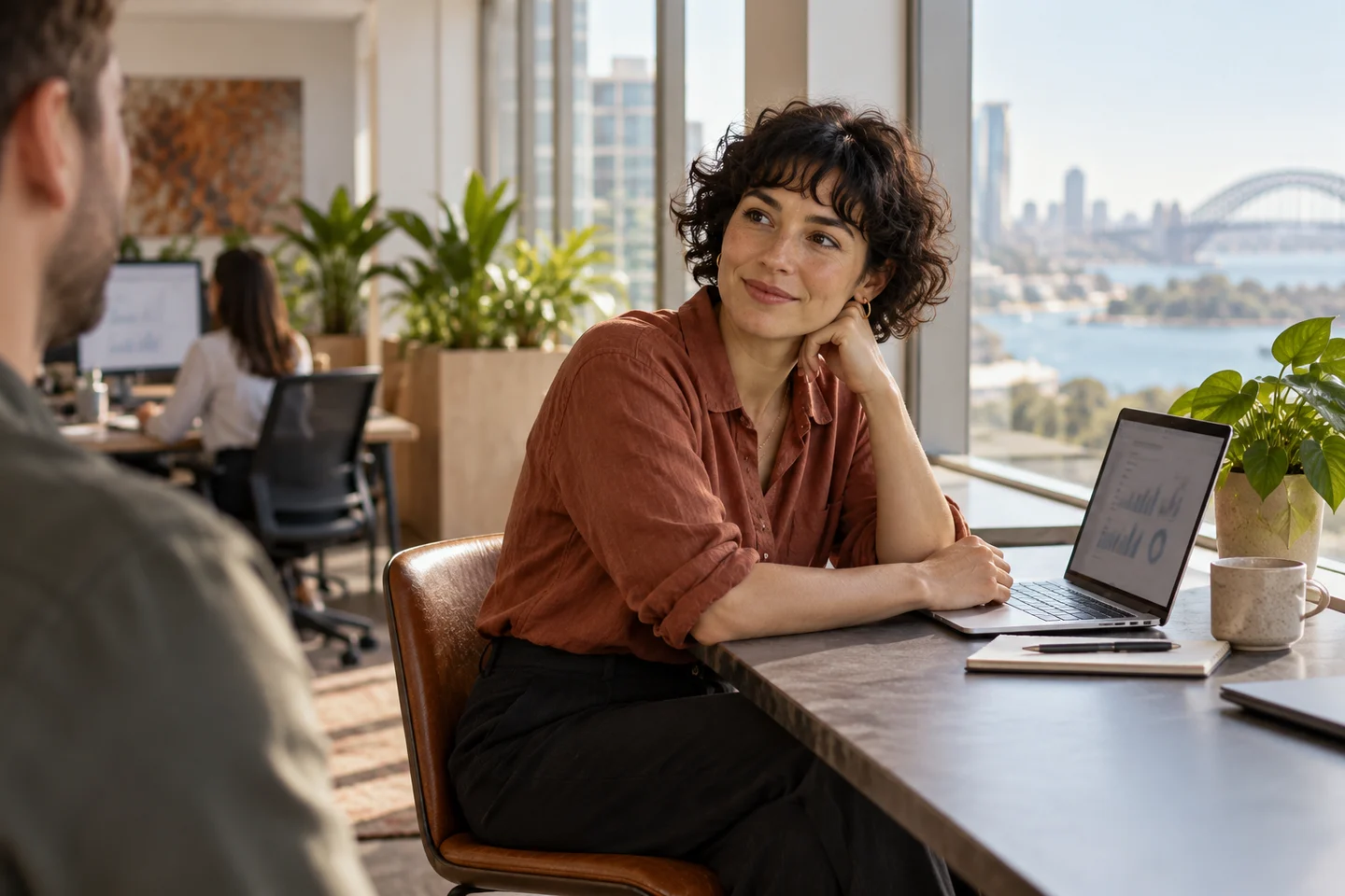 An analyst listens to a colleague at a sunlit office window